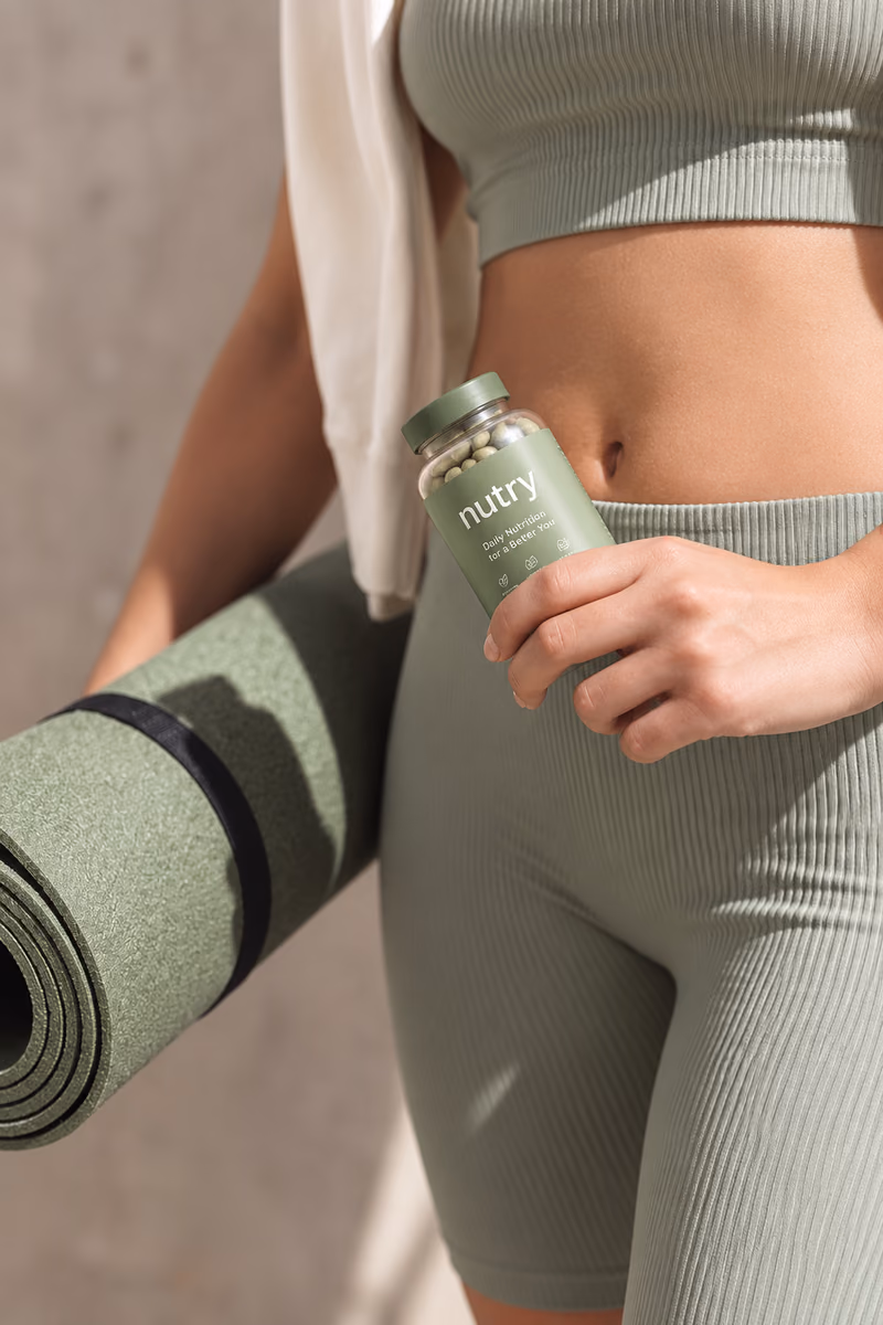 Hand holding a jar of Nutry vitamins against green leggings